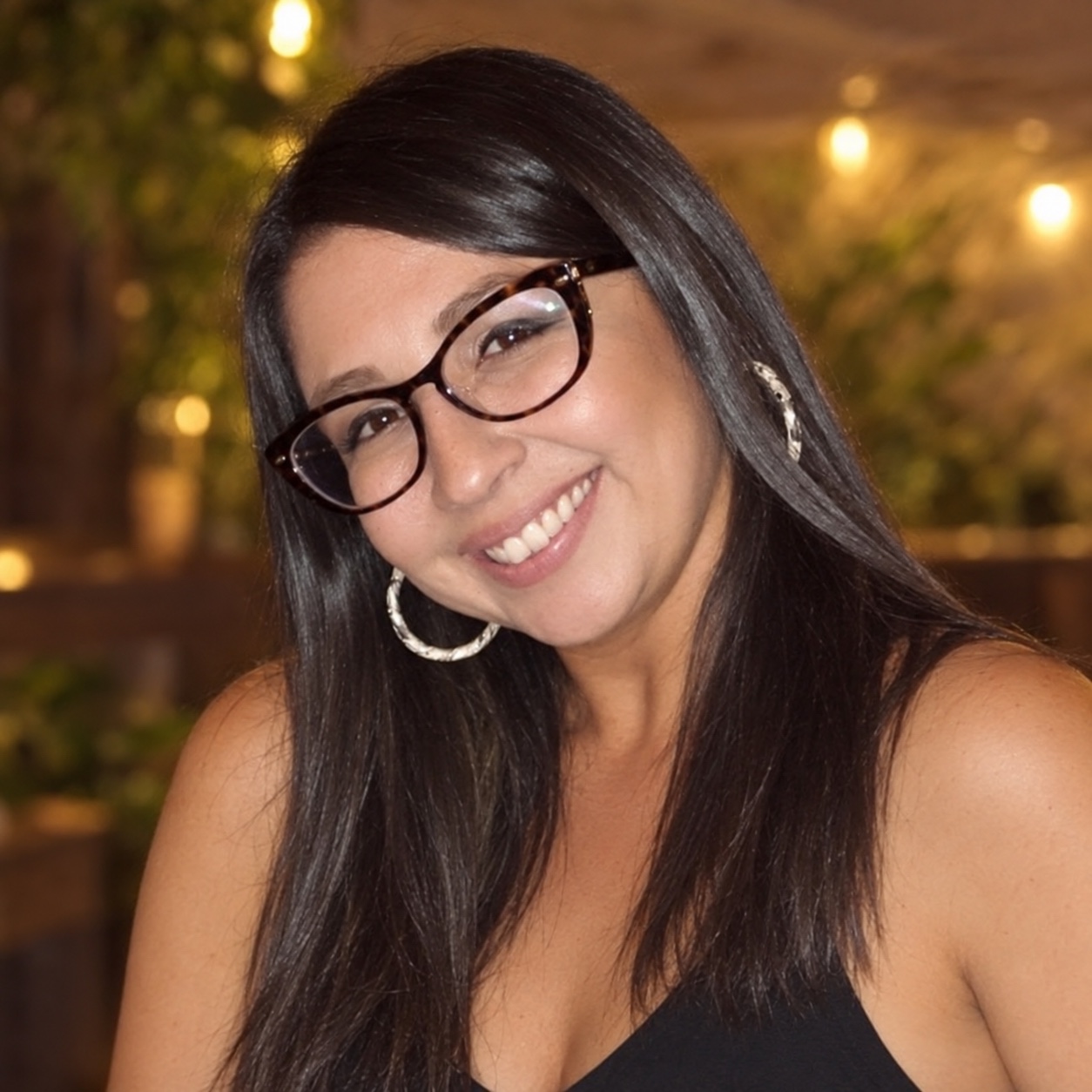 Sweet Ayala smiling, wearing glasses and hoop earrings